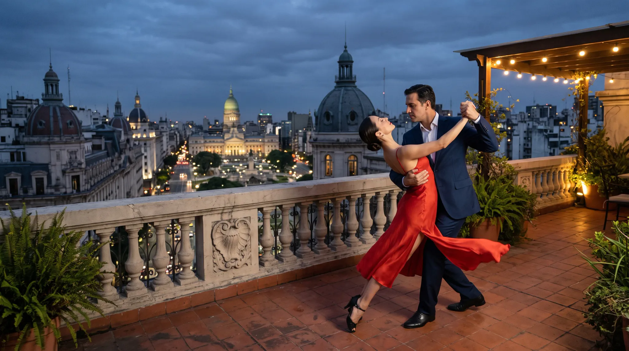 Two adults dance closely on a tiled rooftop terrace overlooking a brightly lit urban skyline with ornate domed buildings. The woman wears a flowing red dress and black heels; the man wears a navy suit with black dress shoes. Warm patio lights and potted greenery create a romantic evening atmosphere.