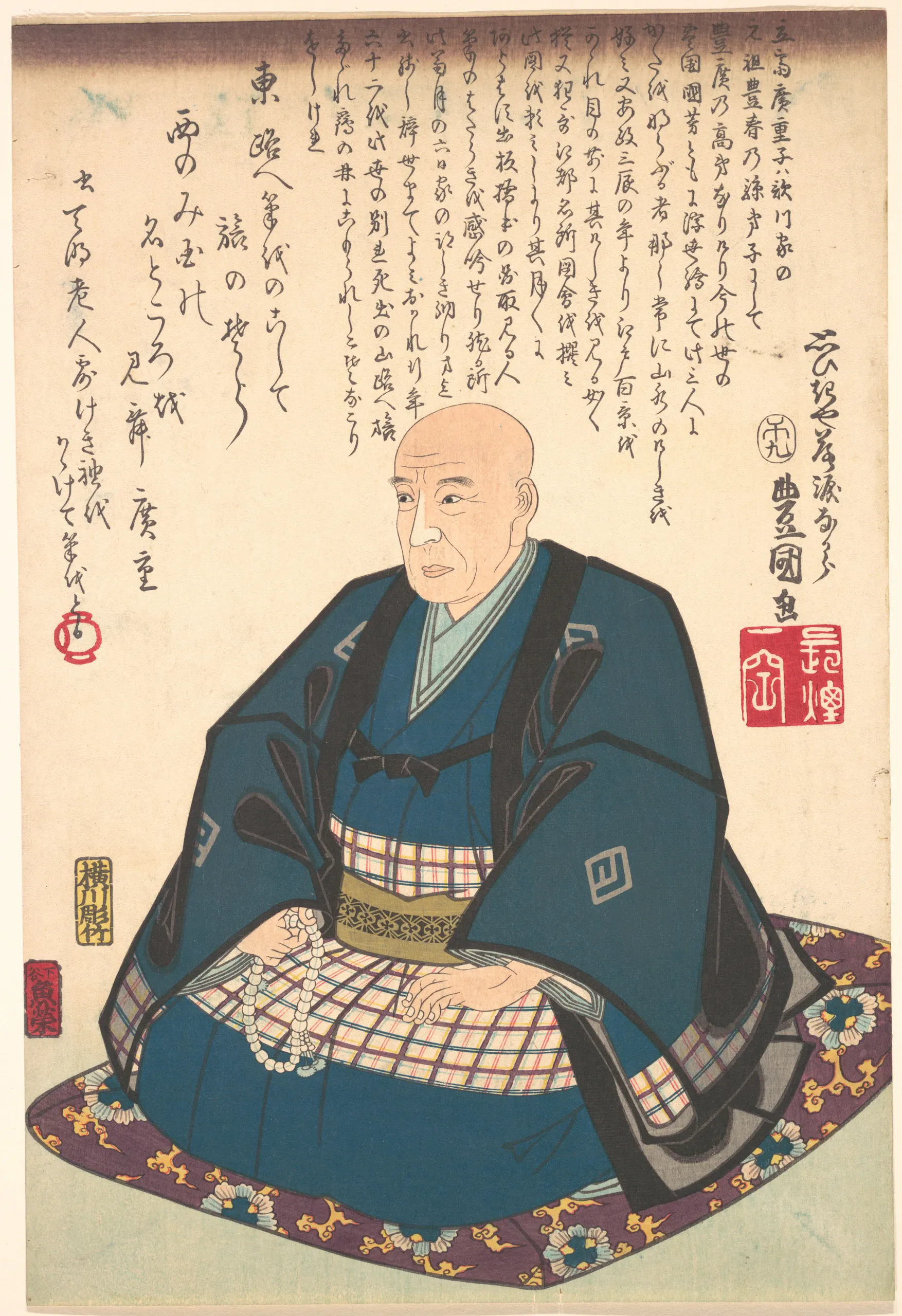 A single bald adult man is shown nearly full-body, seated upright on an ornate purple floral cushion. He wears layered dark blue robes over a pale plaid lower garment with a patterned sash, and holds a loop of prayer beads in his hands. The traditional color print includes extensive handwritten Japanese calligraphy and red seals around the figure.