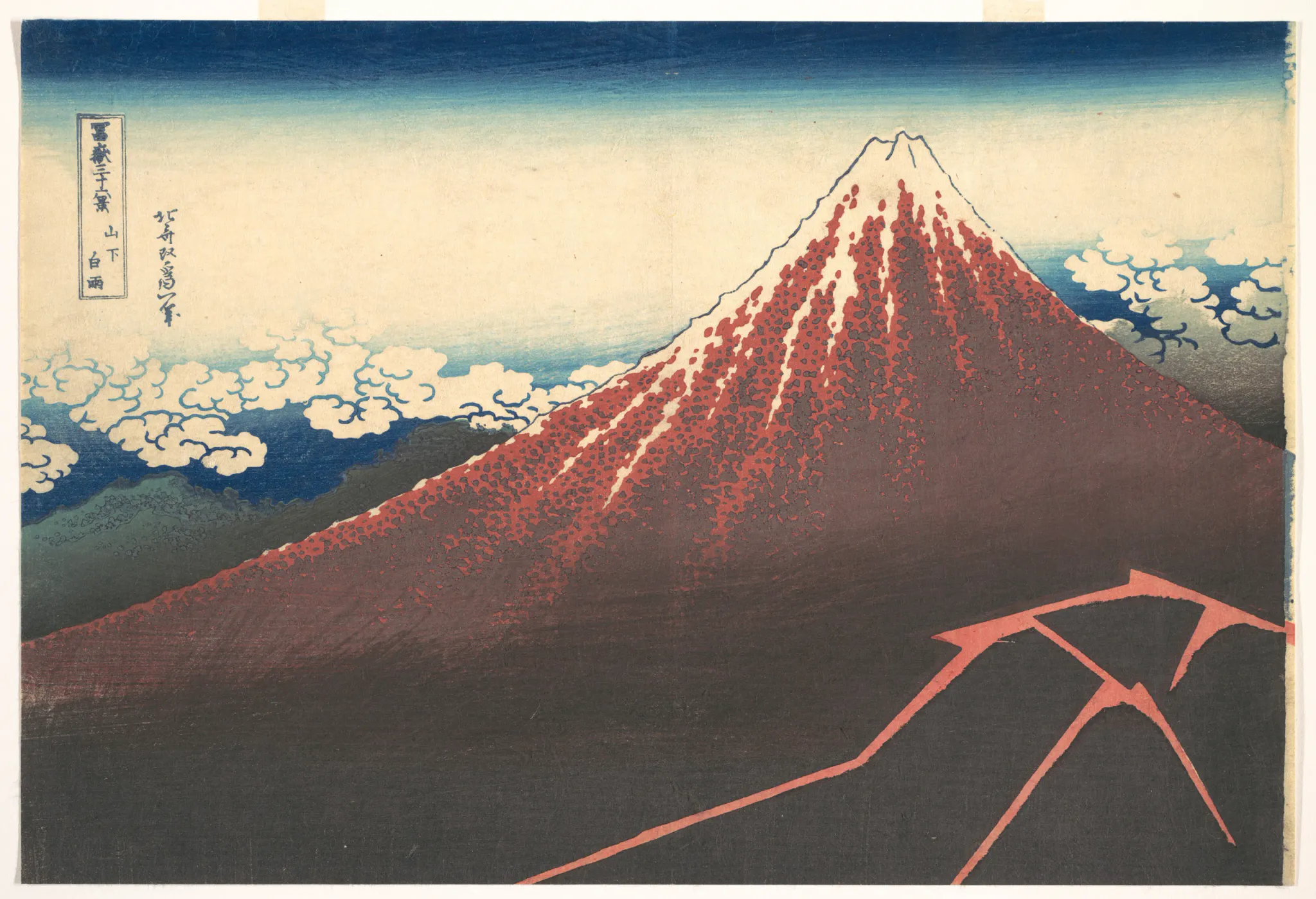 A color Japanese woodblock print depicts a large red volcanic mountain with a snow-covered summit, rising above dark foothills and stylized white clouds. The mountain dominates the right side while open pale sky fills the left; the image has a broad landscape composition and visible print texture.