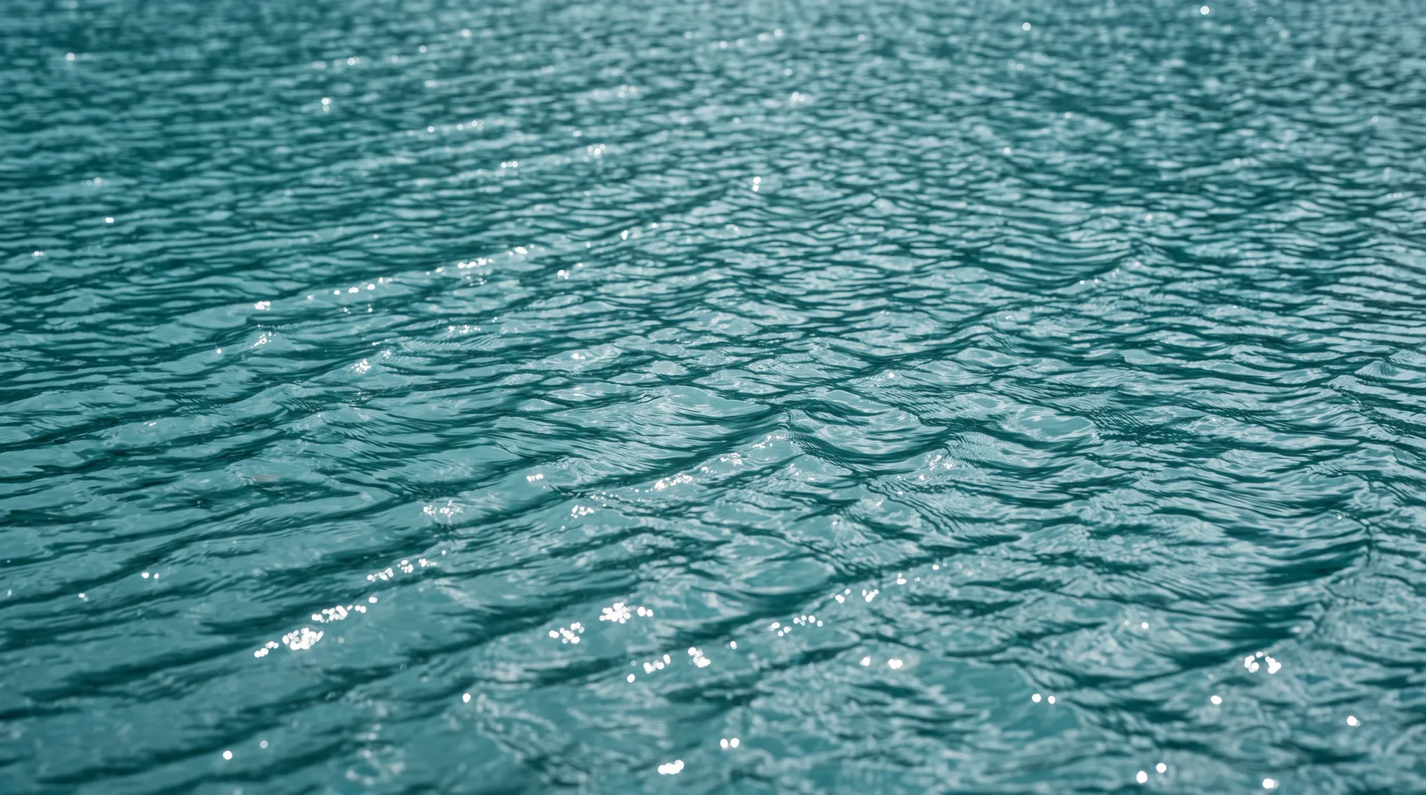 Full-frame close view of rippled teal-blue water, shimmering with bright sunlight reflections. The open water fills the entire landscape composition with no visible shoreline, horizon, sky, people, or built objects.