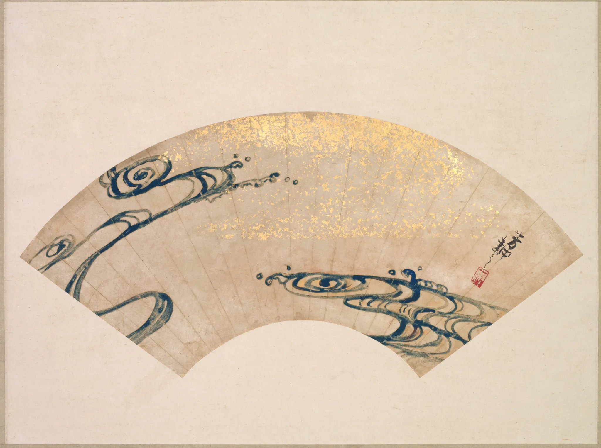An unfolded, fan-shaped artwork on aged beige paper, painted with two stylized blue-green dragon-like reptile figures surrounded by sparse gold decoration. Black calligraphic marks and red seals appear near the right side, with broad neutral negative space around the fan.